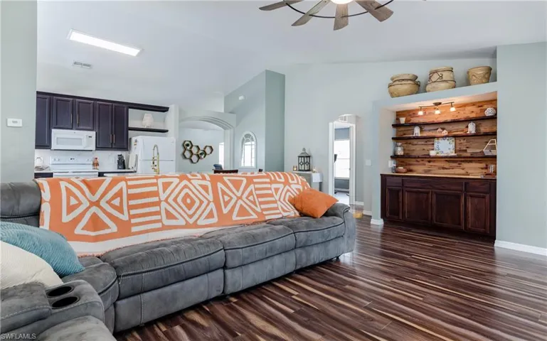 Living room with arched walkways, vaulted ceiling, dark wood finished floors, and ceiling fan