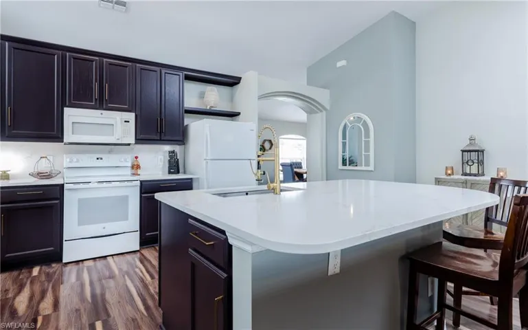 Kitchen featuring white appliances, open shelves, arched walkways, dark wood finished floors, and light stone counters