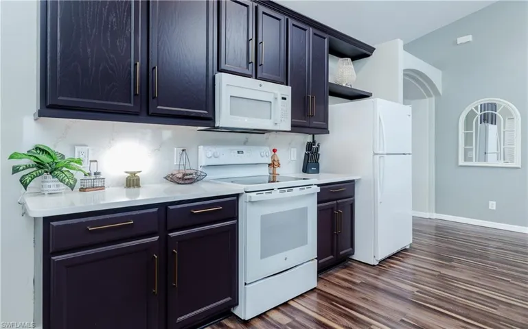 Kitchen with white appliances, dark wood-style flooring, open shelves, and light stone counters