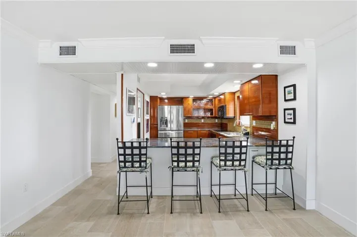 Kitchen featuring dark countertops, tasteful backsplash, recessed lighting, a breakfast bar, and stainless steel fridge with ice dispenser - Virtually Edited Image