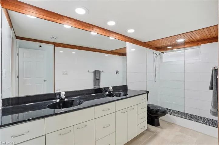 Full bathroom featuring double vanity, tiled shower, recessed lighting, tile walls, and light tile patterned floors - Virtually Edited Image