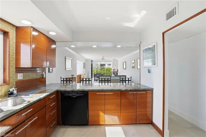 Kitchen featuring dark stone countertops, a peninsula, brown cabinetry, dishwasher, and recessed lighting - Virtually Edited Image