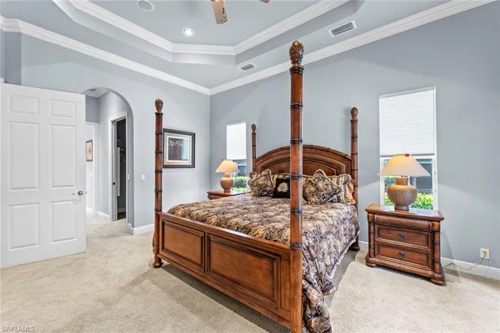 Carpeted bedroom featuring a tray ceiling, ornamental molding, and ceiling fan