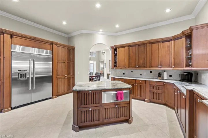Kitchen with light tile floors, backsplash, built in refrigerator, and light stone counters
