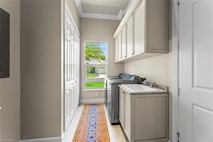 Washroom with cabinets, separate washer and dryer, ornamental molding, sink, and light tile flooring