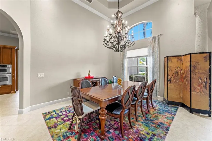 Tiled dining space with a tray ceiling, a notable chandelier, crown molding, and a high ceiling