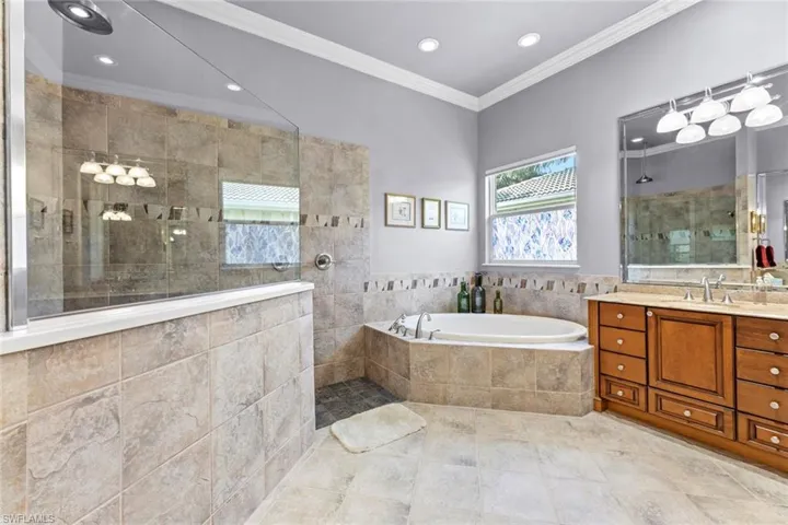 Bathroom with tile floors, shower with separate bathtub, crown molding, and vanity