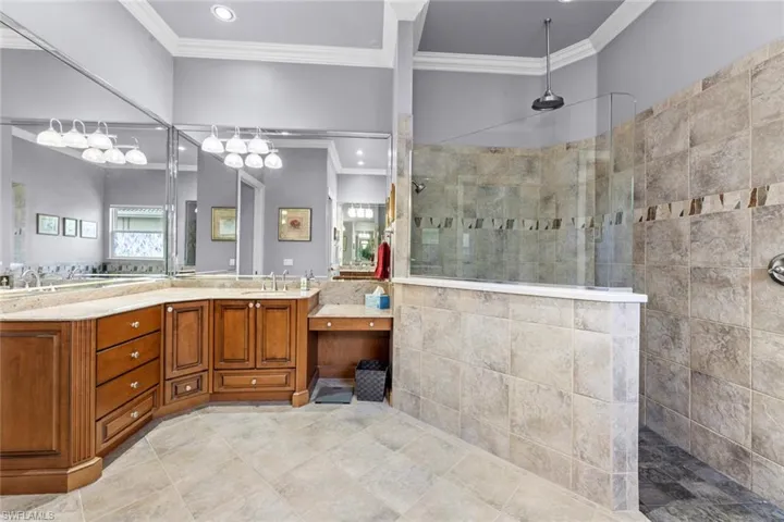 Bathroom featuring a tile shower, double vanity, tile floors, and crown molding
