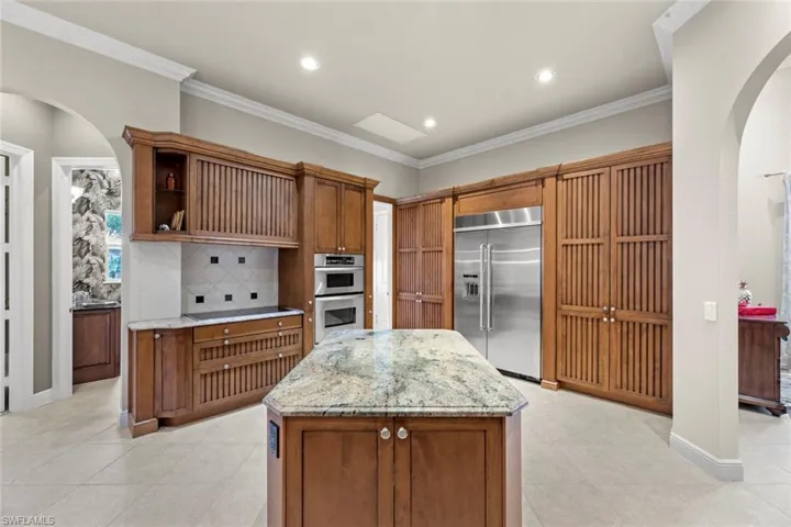 Kitchen with light stone counters, light tile flooring, stainless steel appliances, backsplash, and a center island