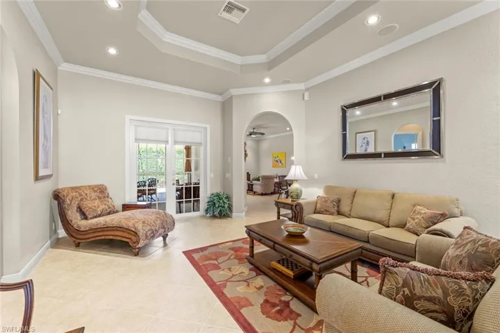 Living room featuring a tray ceiling, crown molding, french doors, and light tile floors