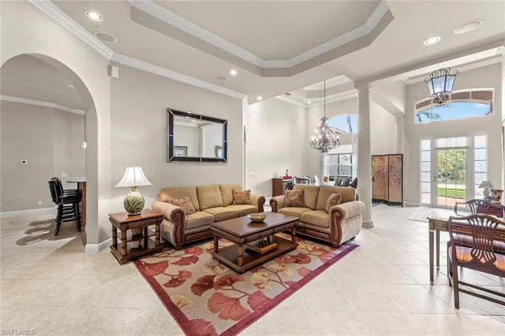Tiled living room with an inviting chandelier, ornate columns, a tray ceiling, and crown molding