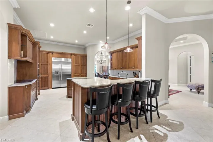 Kitchen with stainless steel built in fridge, kitchen peninsula, light stone counters, pendant lighting, and light tile floors