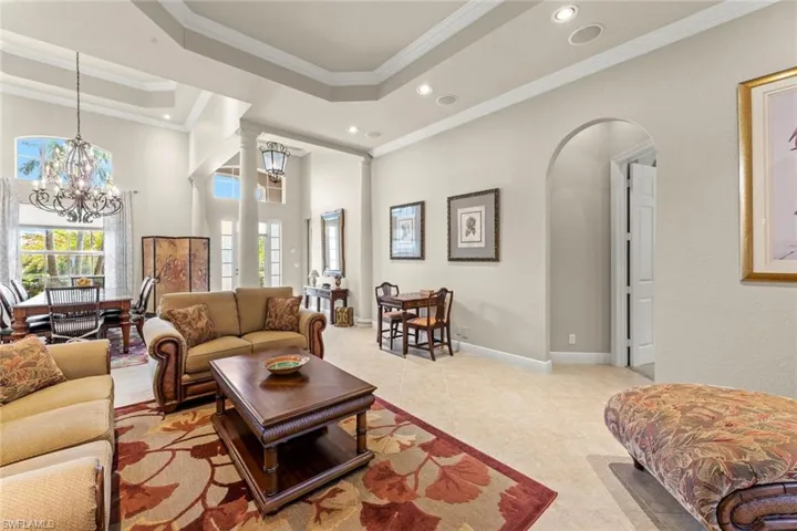 Tiled living room featuring a raised ceiling, a chandelier, and ornamental molding