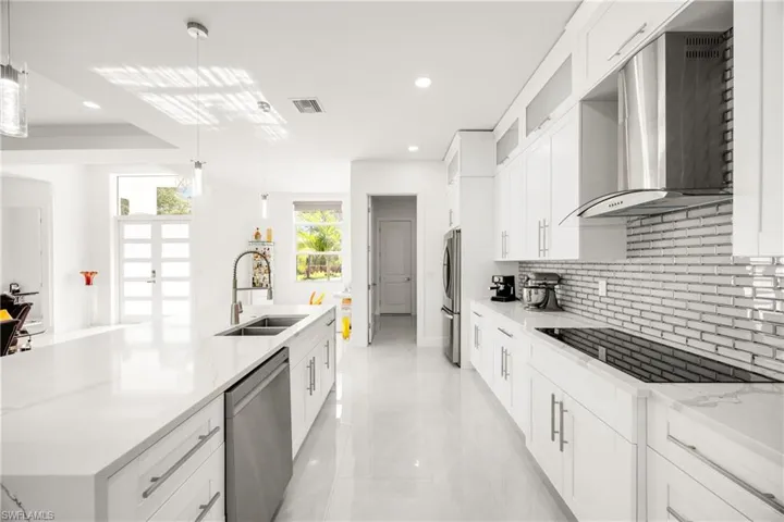 Kitchen with white cabinetry, wall chimney range hood, pendant lighting, light stone countertops, and recessed lighting