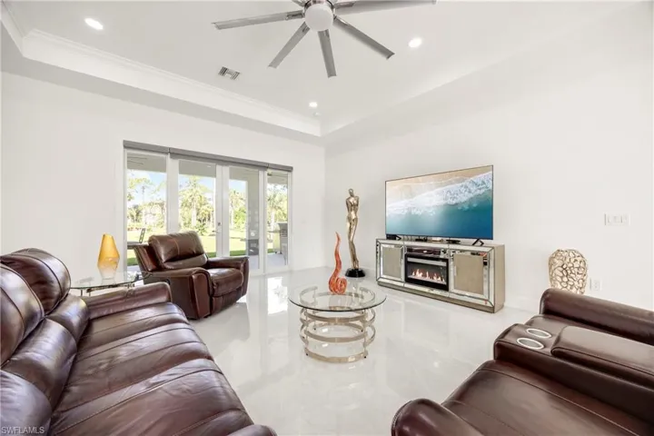 Living room with a raised ceiling, recessed lighting, a lit fireplace, french doors, and a ceiling fan