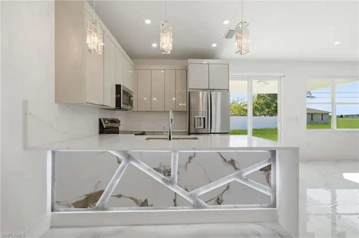 Kitchen with a peninsula, light stone counters, stainless steel appliances, decorative light fixtures, and modern cabinets