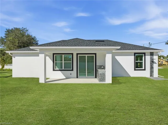 Rear view of house with a yard, a patio area, stucco siding, and a shingled roof