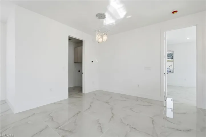 Spare room with light marble finish floors and a chandelier
