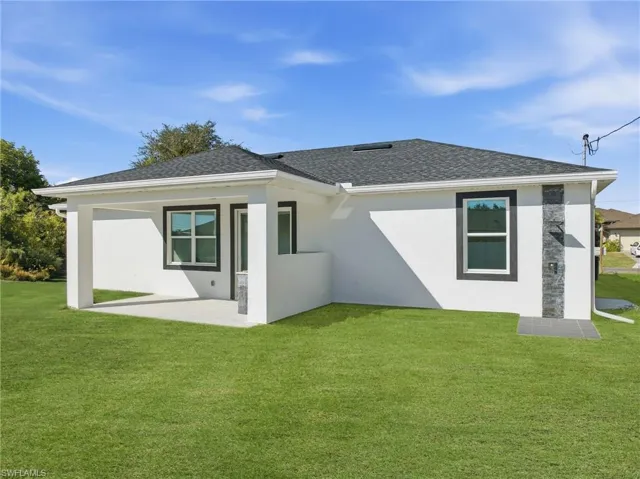 Rear view of house featuring a yard, a patio, stucco siding, and a shingled roof