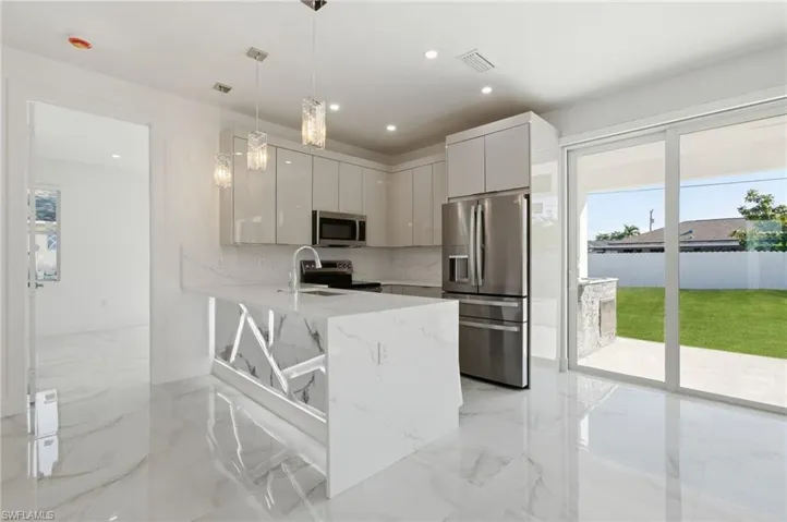 Kitchen with a peninsula, appliances with stainless steel finishes, modern cabinets, decorative light fixtures, and light stone countertops