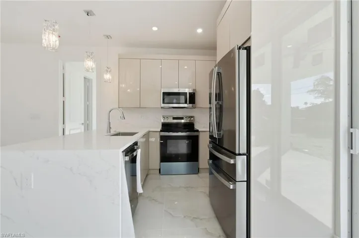 Kitchen featuring stainless steel appliances, a peninsula, pendant lighting, light stone counters, and modern cabinets