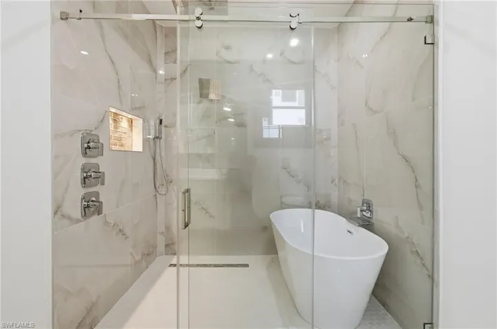 Bathroom with a freestanding bath, a marble finish shower, tile walls, and healthy amount of natural light