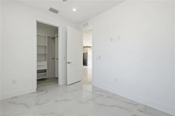 Unfurnished bedroom featuring a spacious closet, stainless steel refrigerator with ice dispenser, recessed lighting, and light marble finish flooring