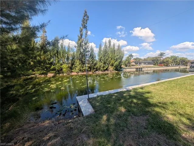 Waterfront property featuring a concrete seawall, lush green lawn, mature trees, and a clear blue sky