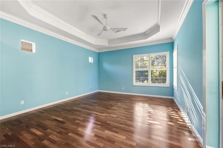 Spare room with dark wood-style flooring, a ceiling fan, crown molding, and a raised ceiling