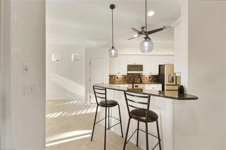 Kitchen featuring a kitchen breakfast bar, tasteful backsplash, white cabinets, dark stone counters, and stainless steel refrigerator with ice dispenser