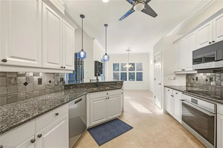 Kitchen with backsplash, dark stone countertops, white cabinets, ornamental molding, and stainless steel appliances