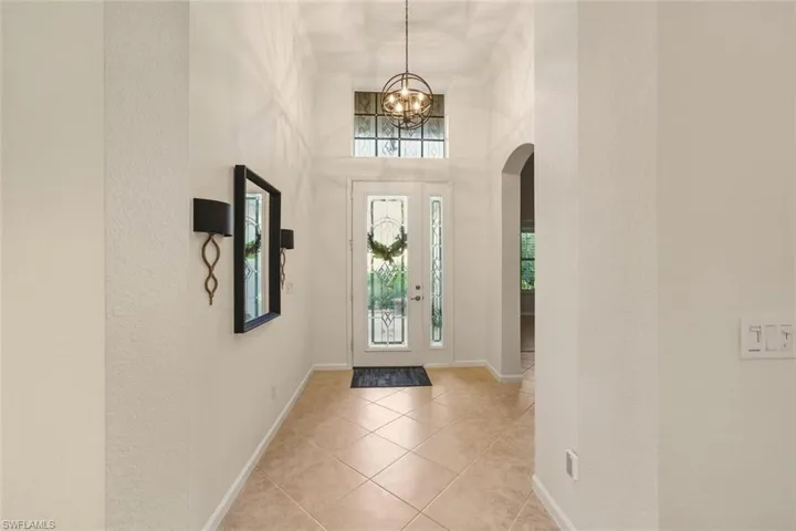 Entryway featuring a textured wall, arched walkways, a high ceiling, and light tile patterned flooring