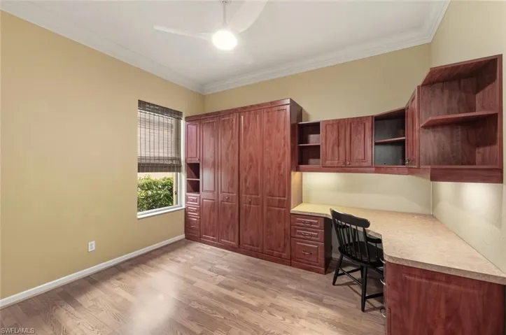 Unfurnished office with built in study area, ornamental molding, light wood-style floors, and a ceiling fan