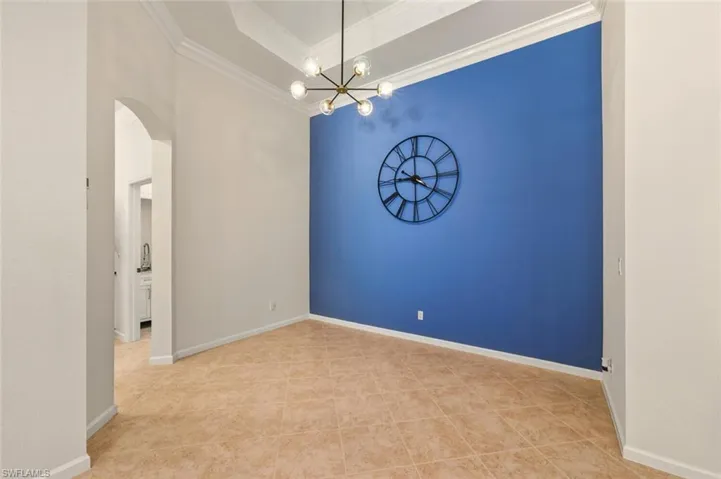 Empty room featuring arched walkways, a chandelier, ornamental molding, and light tile patterned floors