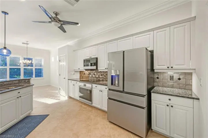 Kitchen with white cabinets, appliances with stainless steel finishes, dark stone counters, ornamental molding, and decorative light fixtures