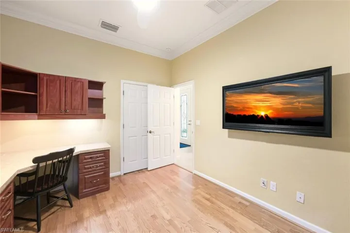 Office space with built in study area, light wood-style floors, and crown molding