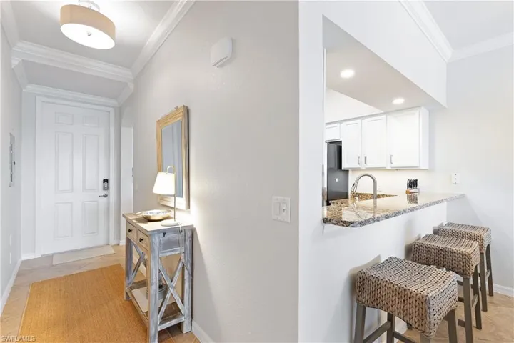 Kitchen featuring kitchen peninsula, ornamental molding, light stone counters, white cabinetry, and a breakfast bar area