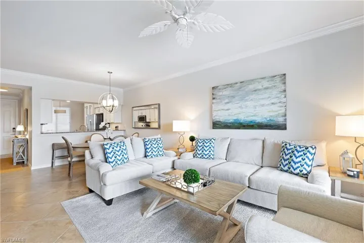 Tiled living room with ceiling fan with notable chandelier and ornamental molding