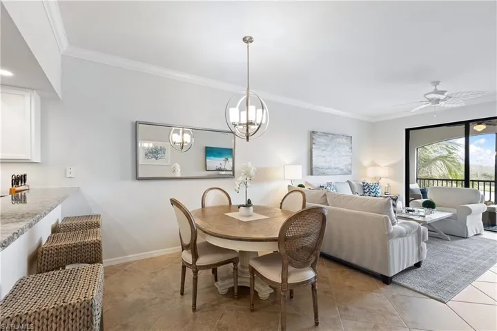 Dining space with light tile patterned floors, ceiling fan with notable chandelier, and crown molding