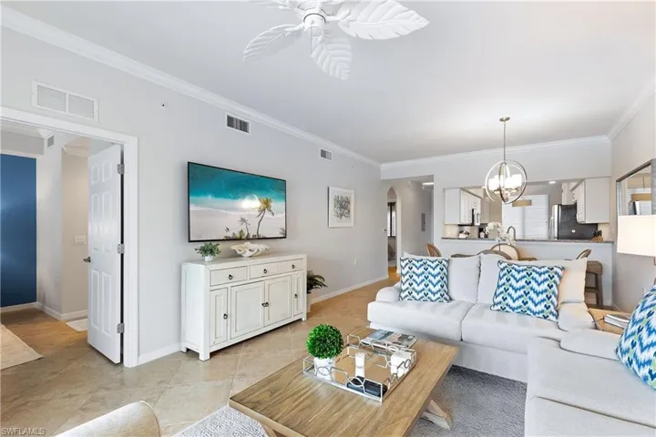 Living room with light tile patterned floors, ceiling fan with notable chandelier, and ornamental molding