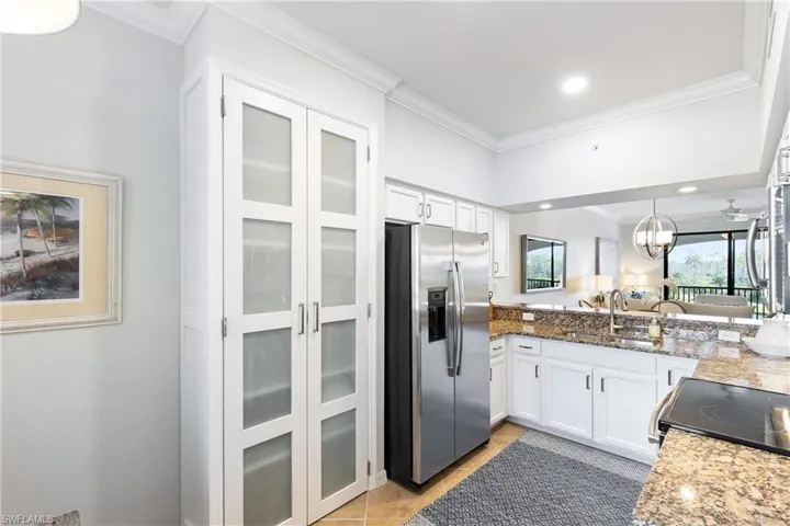 Kitchen with stainless steel fridge, light stone countertops, white cabinetry, and sink