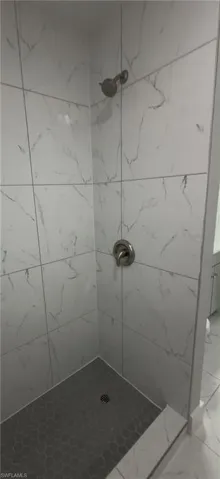 Shower stall featuring large format white tile with gray veining, a matte gray hexagonal tile floor, and brushed nickel fixtures