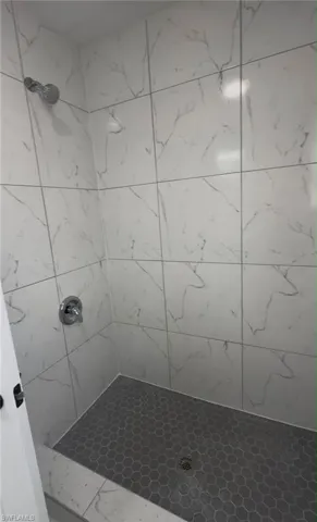 Shower stall with large format white tiled walls featuring grey veining, grey hexagonal floor tiling, and a chrome shower head and fixtures