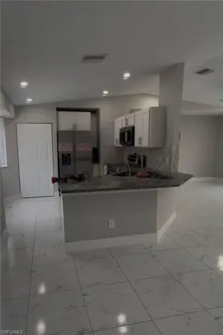 Kitchen featuring an extended peninsula with a stone countertop, white shaker cabinetry, stainless steel refrigerator, and recessed lighting