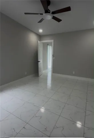 Spacious room featuring large format white tile flooring with veining, neutral gray walls, and recessed lighting