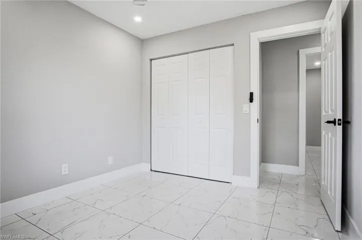 Bright interior space featuring large format marble-look tile flooring, white baseboards, and a bi-fold closet door