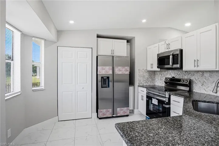 Kitchen featuring white cabinetry, granite countertops, stainless steel appliances, a herringbone tile backsplash, and white tile flooring