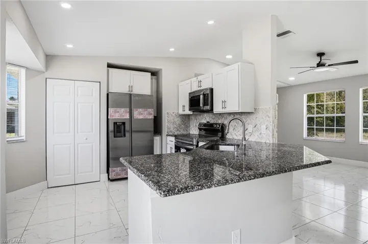 Kitchen featuring an island with a speckled countertop, white cabinetry with dark hardware, stainless steel appliances, and a tiled backsplash
