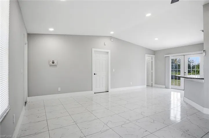 Spacious room featuring vaulted ceilings, recessed lighting, large format tile flooring, and double French doors opening to outdoor green space