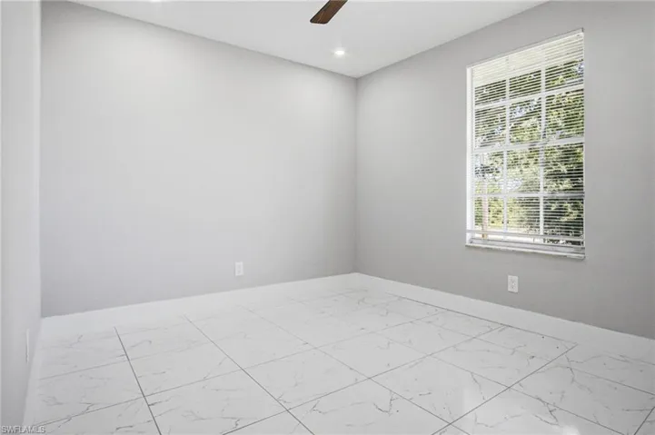 Room featuring large format white tile flooring, neutral wall paint, and a window with horizontal blinds